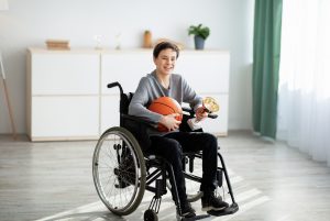 Garoto cadeirante segurando uma bola de basquete e uma taça